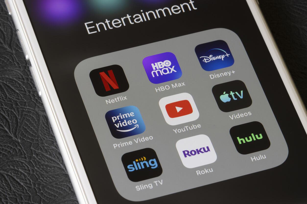 Ein Smartphone-Bildschirm zeigt einen Ordner mit dem Titel „Entertainment“, der verschiedene Streaming-Apps enthält, darunter Netflix, HBO Max, Disney+, Prime Video, YouTube, Apple TV, Sling TV, Roku und Hulu.