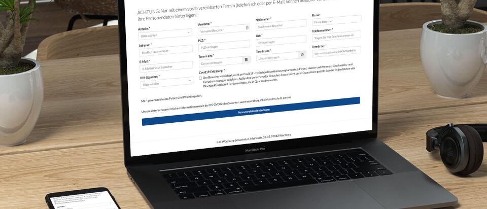 Lap Top steht auf einem Tisch zwischen einem Smartphone und Kopfhörern