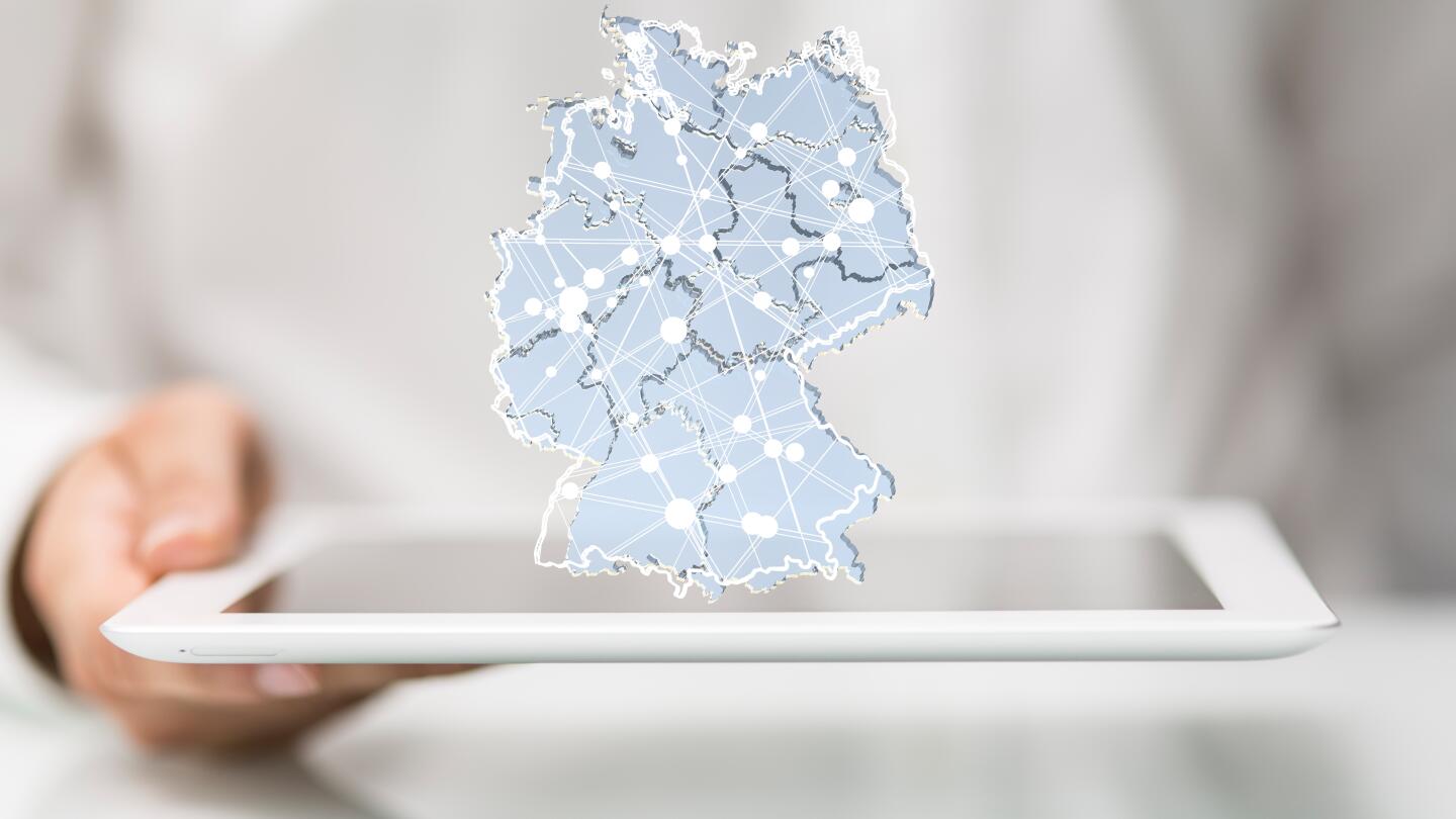 Eine Person hält ein Tablet, über dem eine digitale, vernetzte Deutschlandkarte schwebt.