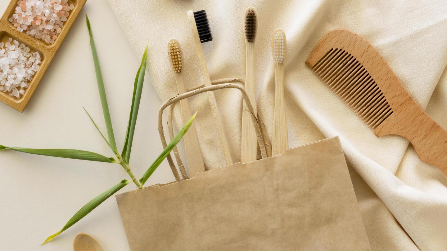Mehrere Bambus-Zahnbürsten und ein Bambuskamm liegen auf einer umweltfreundlichen Papiertüte.