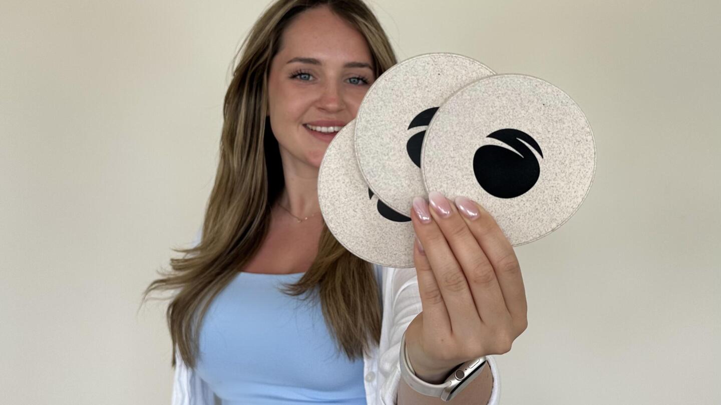 The author, Mia, holds a round, white desktop charging station made from recycled housing, a sustainable tech giveaway