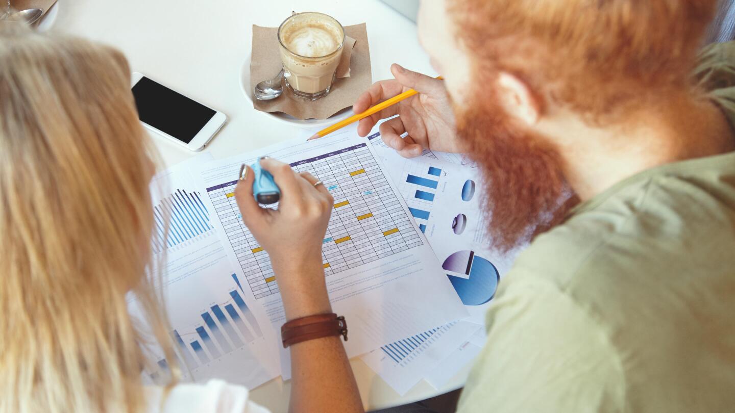 Zwei Personen sitzen an einem Schreibtisch und analysieren gemeinsam ausgedruckte Diagramme und Tabellen.