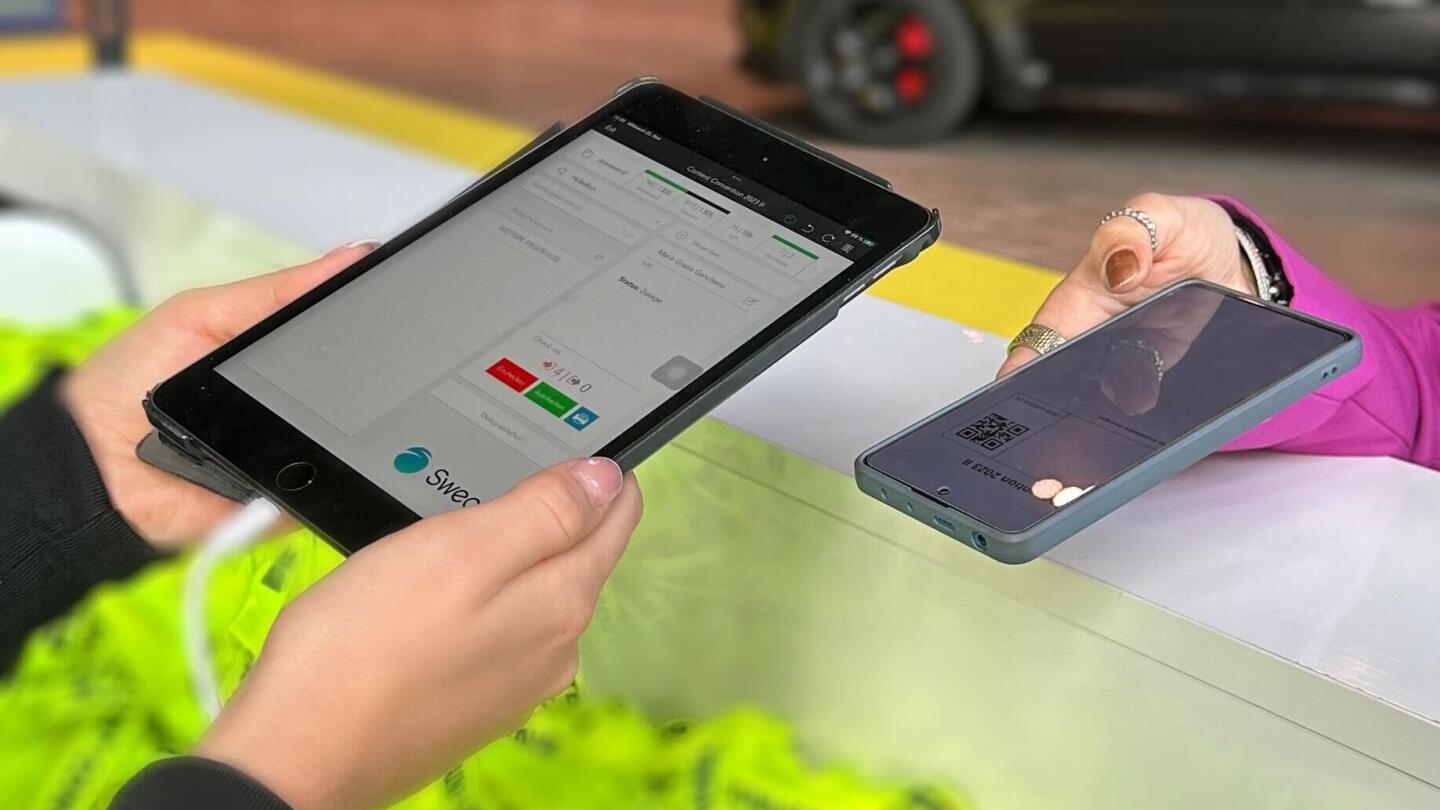 Eine Person hält ein Smartphone mit einem QR-Code an ein Tablet am Event-Check-in, auf dem die Sweap-Software läuft.