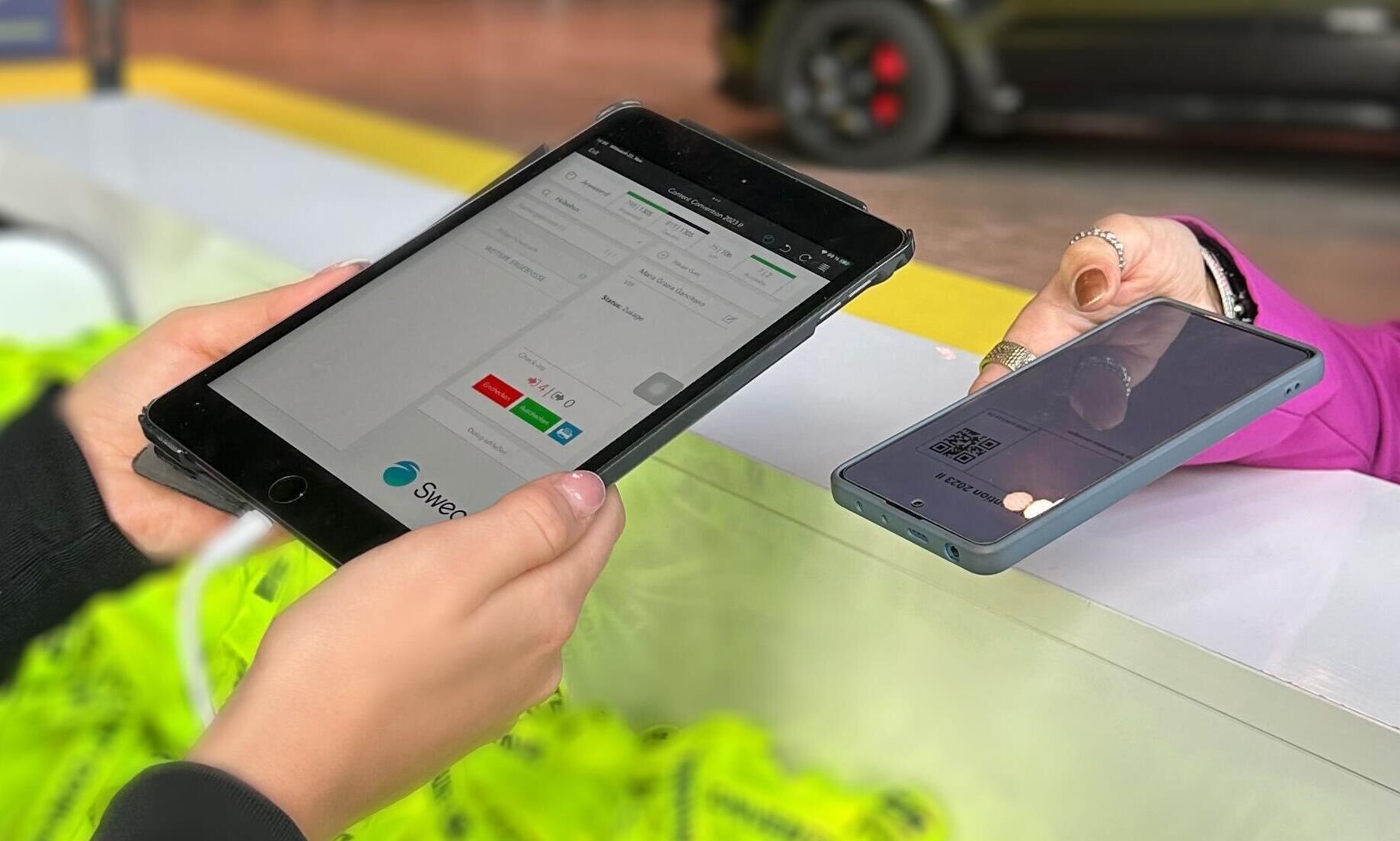 Eine Person hält ein Smartphone mit einem QR-Code an ein Tablet am Event-Check-in, auf dem die Sweap-Software läuft.