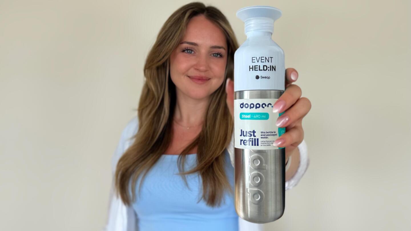 Mia from Sweap holds a reusable, Cradle to Cradle certified water bottle made of recycled steel with ‘EVENT HERO’ printed on it.
